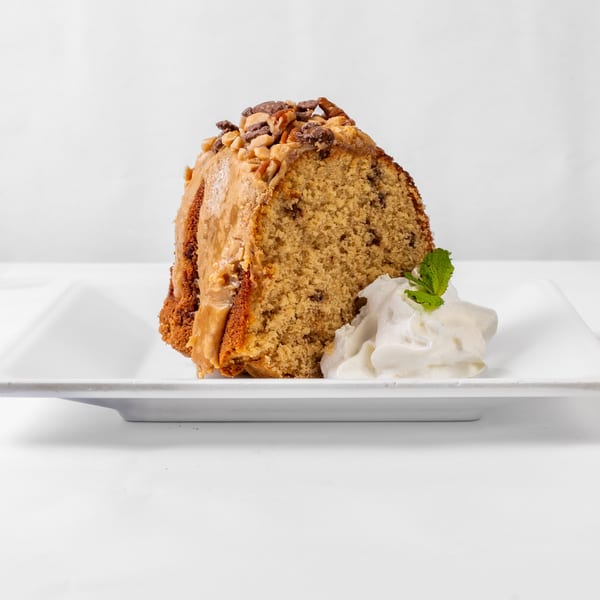 A slice of My 2 Cents LA's bundt cake with caramel, nuts, and whipped cream.