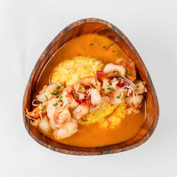 My 2 Cents LA's shrimp and grits, garnished with chives and shredded cheese, in a wooden bowl.