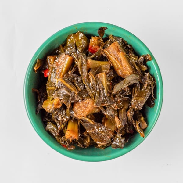 Overhead view of a vibrant green bowl filled with dark, stewed collard greens and red peppers.