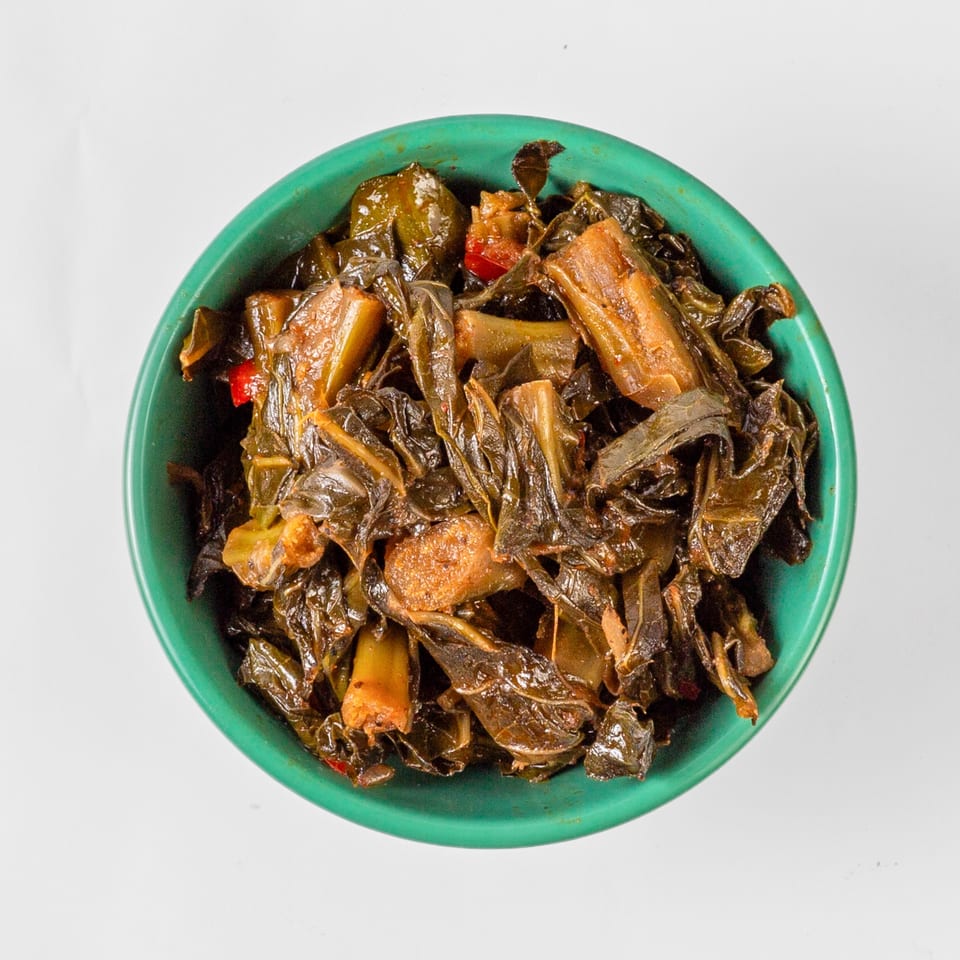 Overhead view of a vibrant green bowl filled with dark, stewed collard greens and red peppers.