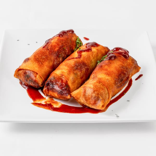 Three crispy, golden-brown soul food egg rolls drizzled with a rich red sauce on a white plate.